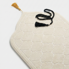 White textured mat with a tassel and black prayer beads on a light gray background